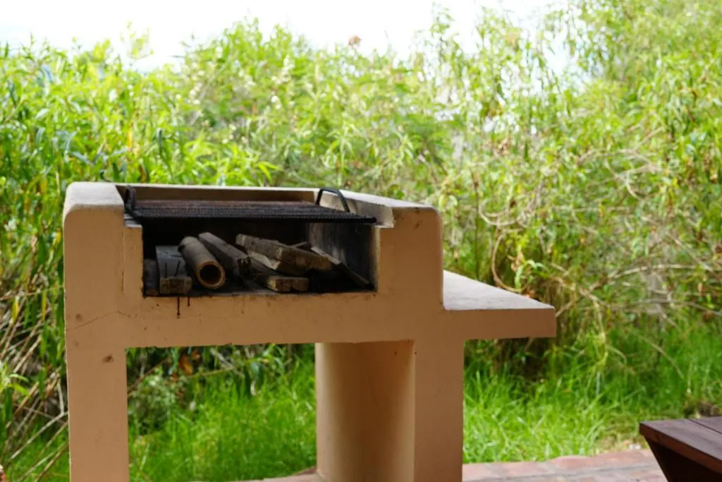 Asador de ladrillo blanco con leña, entre el pasto alto