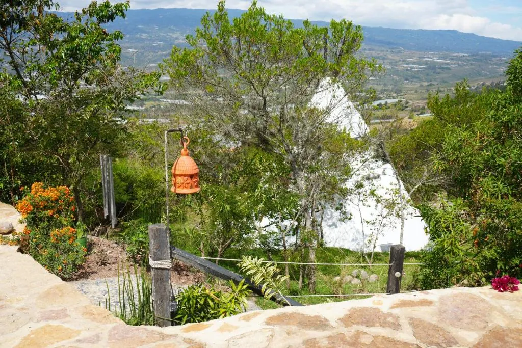 Tipi blanco detrás del jardín, con farol naranja y el valle al fondo