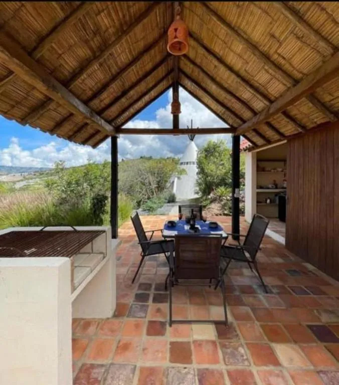 Kiosco de techo de caña con mesa y sillas, abierto al paisaje