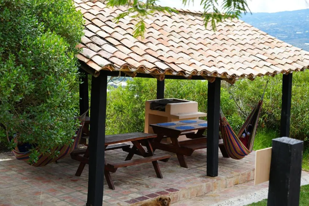 Kiosco de teja con mesas de madera y hamaca, mirando a la montaña